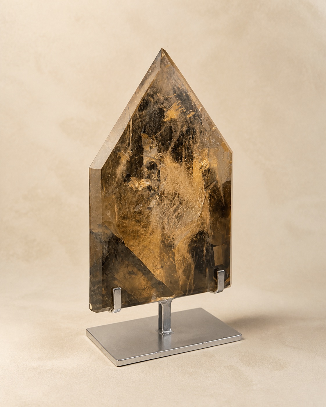 Broad smoky quartz shield sculpture displayed on a dark pedestal