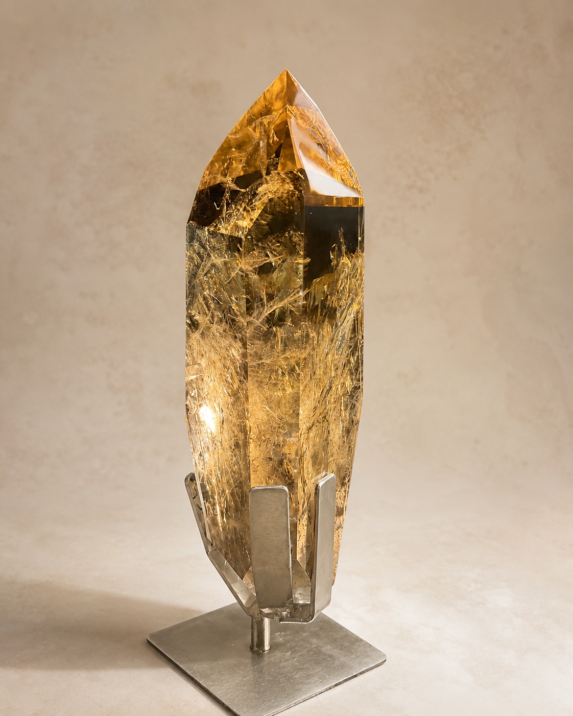 Warm-toned elongated quartz point sculpture displayed on a dark pedestal